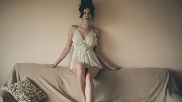 Photo of Beautiful Woman in White Night Dress Sitting on Top of Sofa Backrest